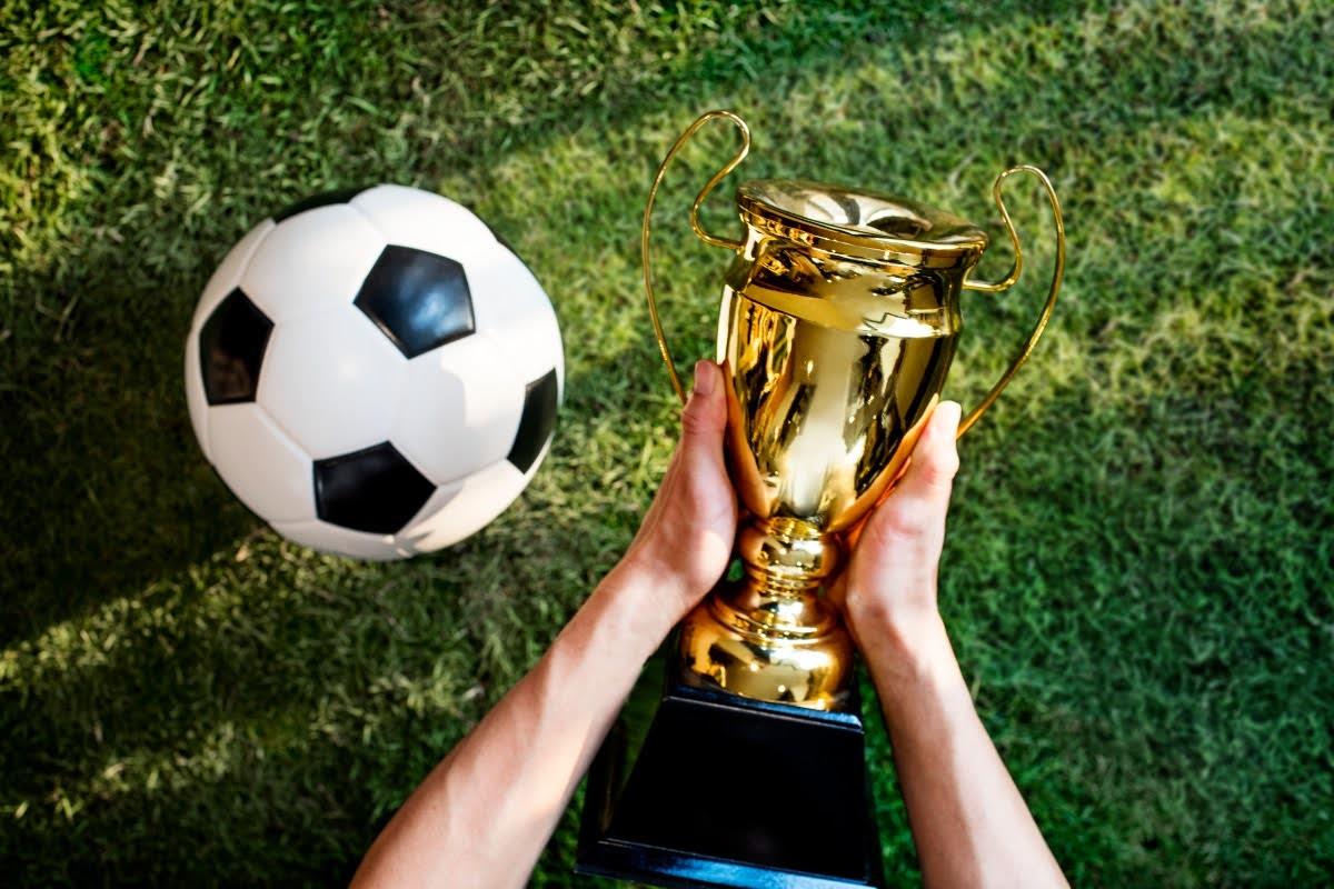 Golden cup held beside a soccer ball, representing the most prestigious soccer trophies.