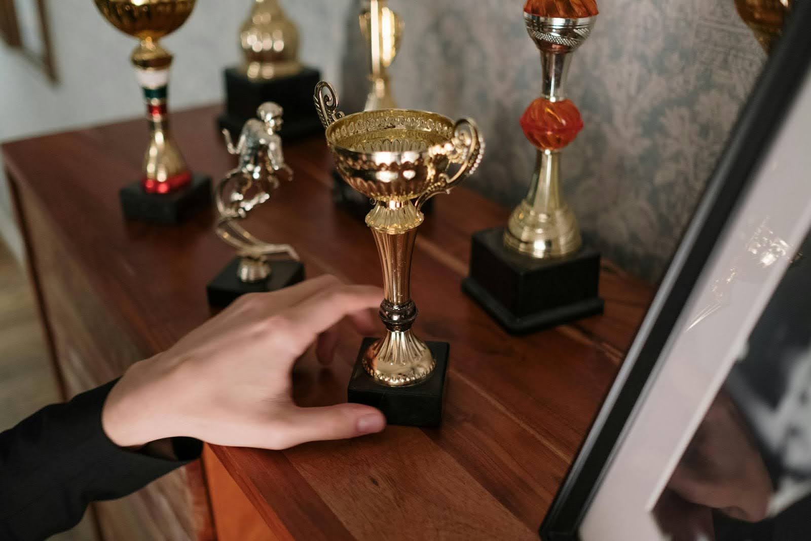 A person moving one of the trophies on a shelf.